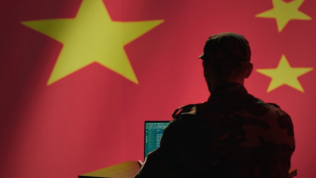 A man sits in front of a computer and the Chinese flag.